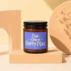 Amber candle with black lid and blue label reading "Our Only Happy Place Vowed".