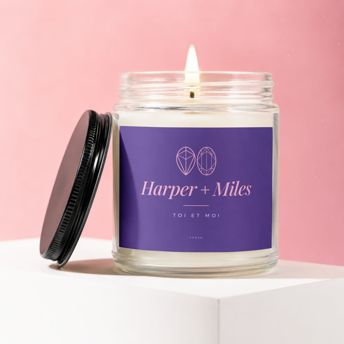 Glass jar candle with lit wick and purple label reading "Harper + Miles TOI ET MOI VOWED".