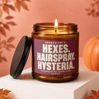 Amber glass candle with lit wick and "Hexe, Hairspray, Hysteria" label.