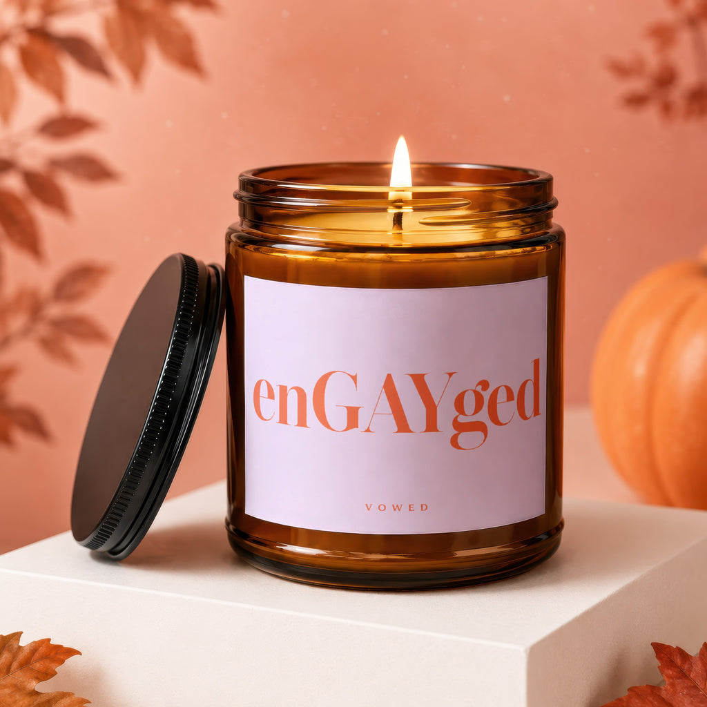 Amber jar candle with lit wick, "enGAYged" text, and pumpkin decoration.