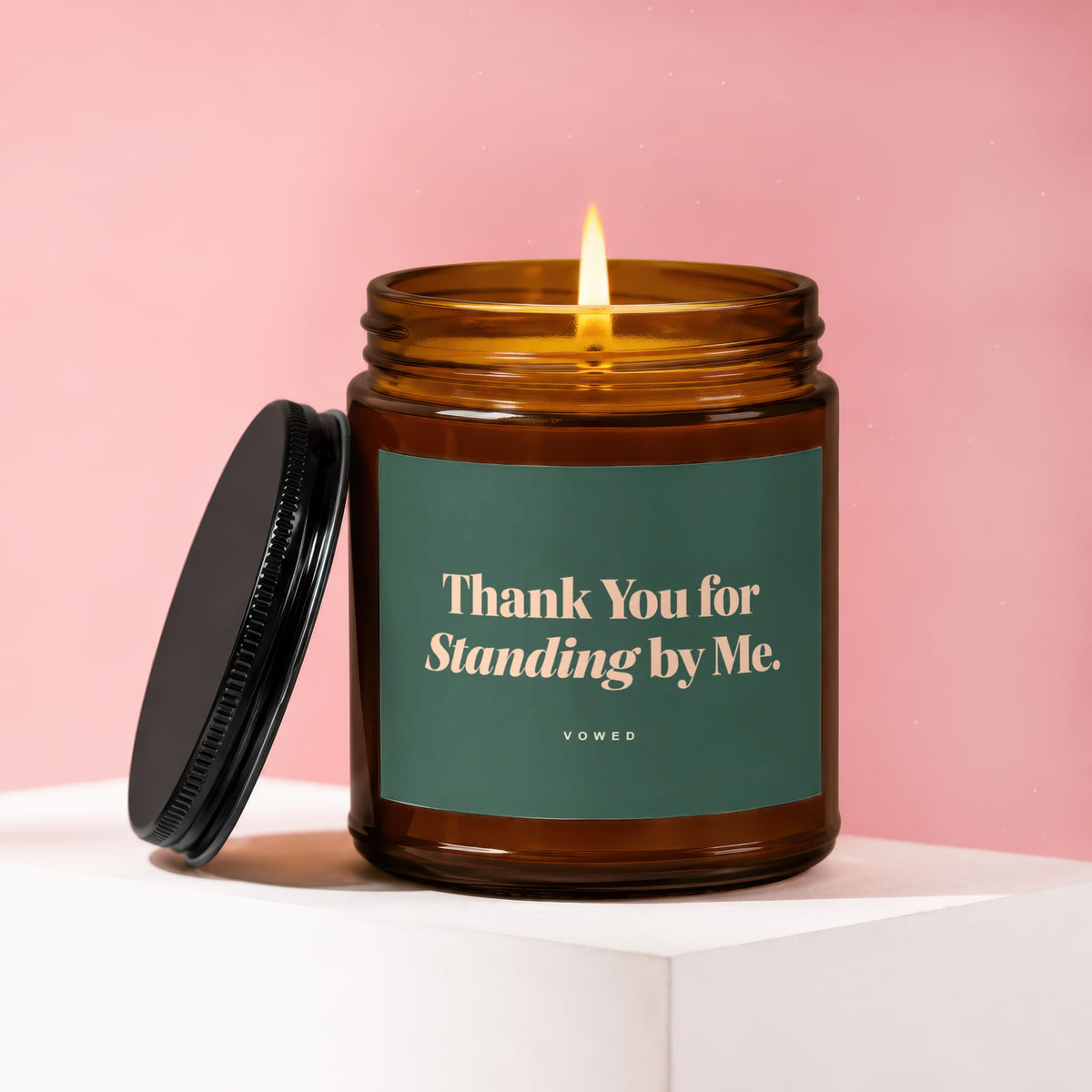 Amber glass candle with lit wick, green label reading "Thank You for Standing by Me. VOWED."