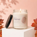 Candle with "here's to forever" text and leaf design, lid off.