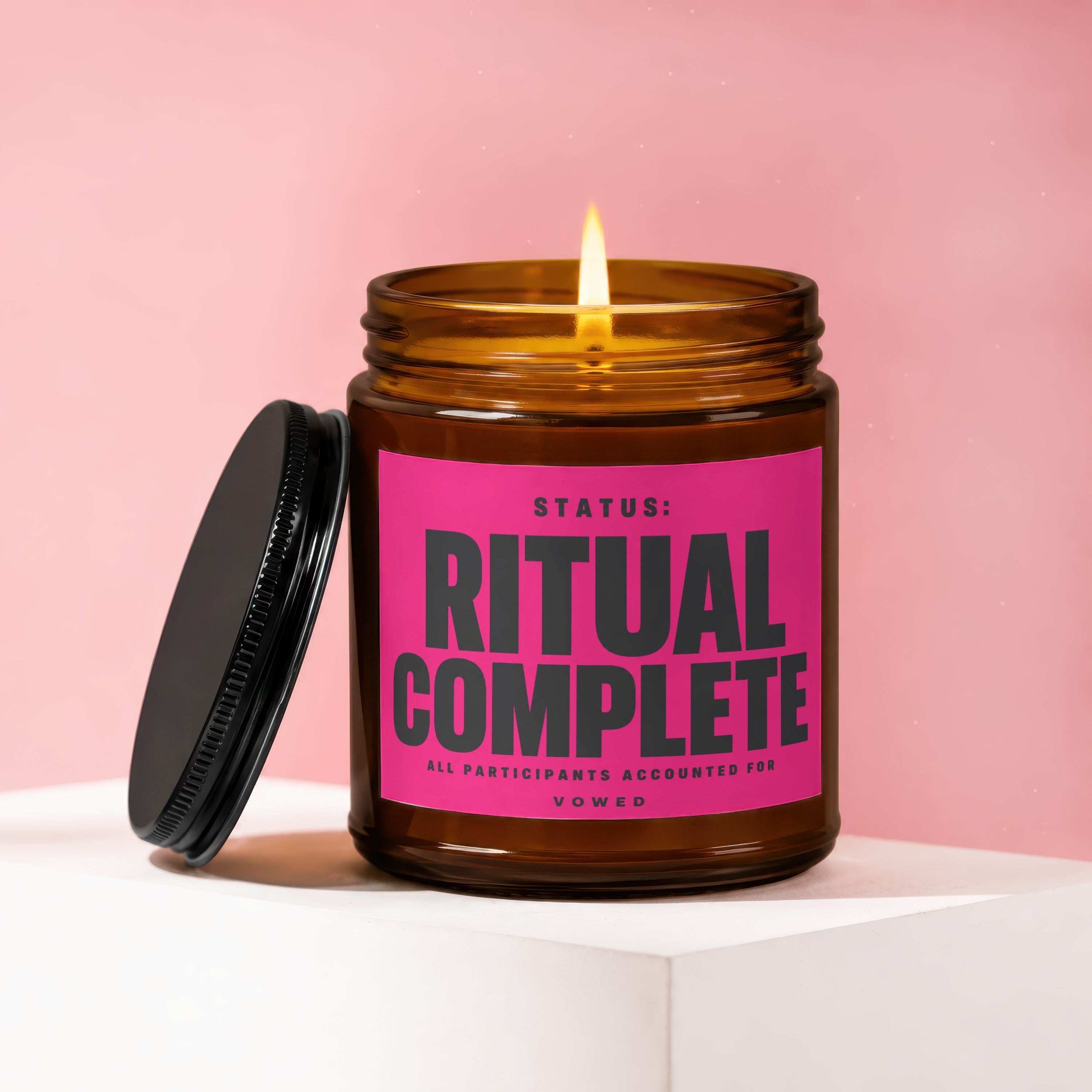 Amber candle with lit flame, pink label reads "STATUS: RITUAL COMPLETE"