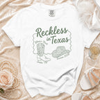 White t-shirt with "Reckless in Texas" text, cowboy boots, and hat graphic.