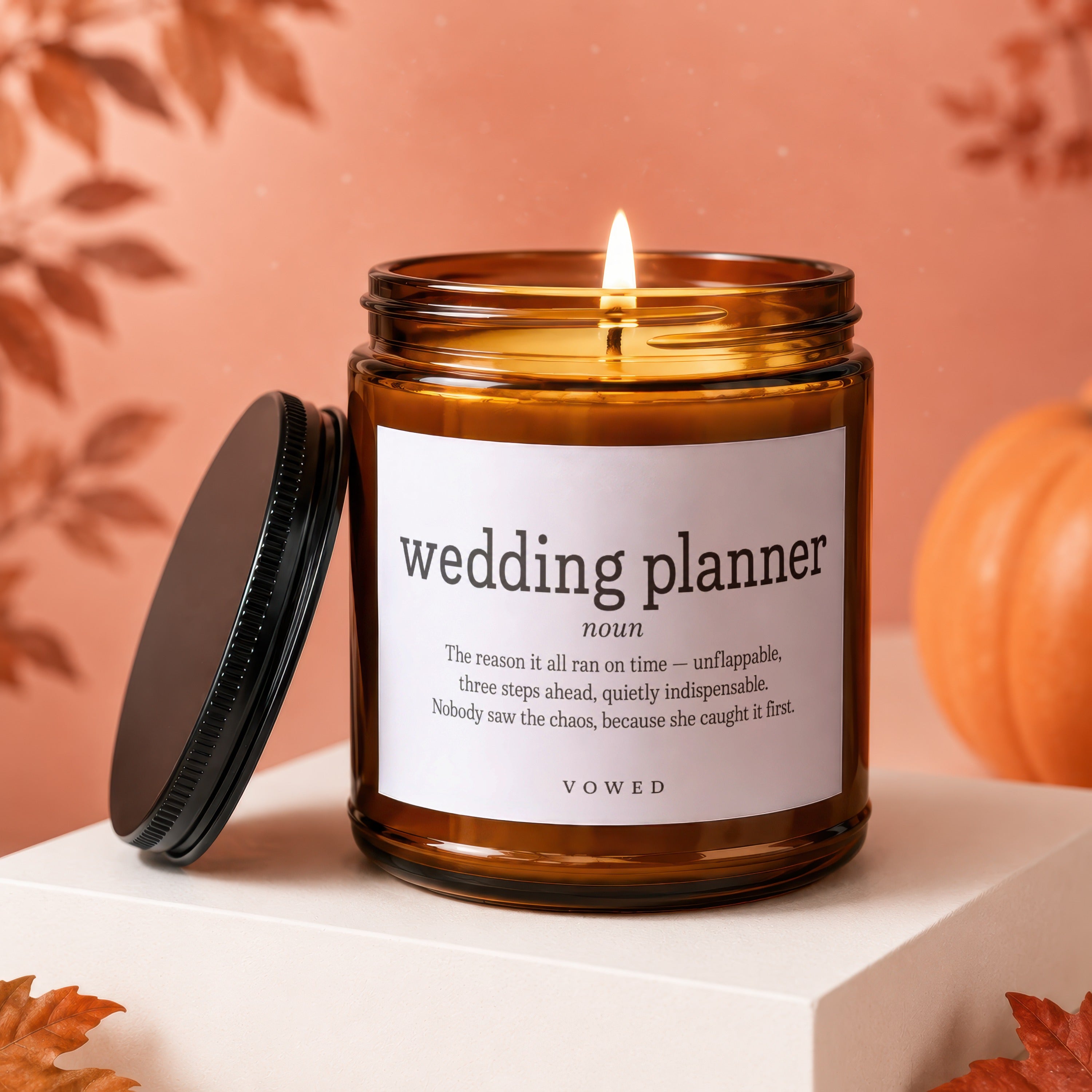 Candle with "wedding planner" text definition with autumn leaves and pumpkin decor.