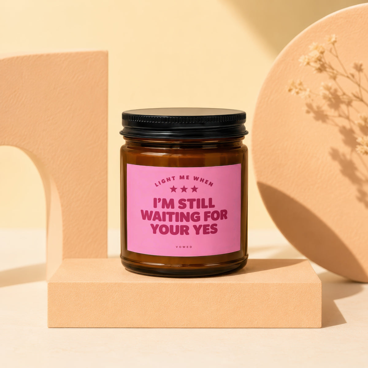 Brown glass candle with pink label reading "I'M STILL WAITING FOR YOUR YES".