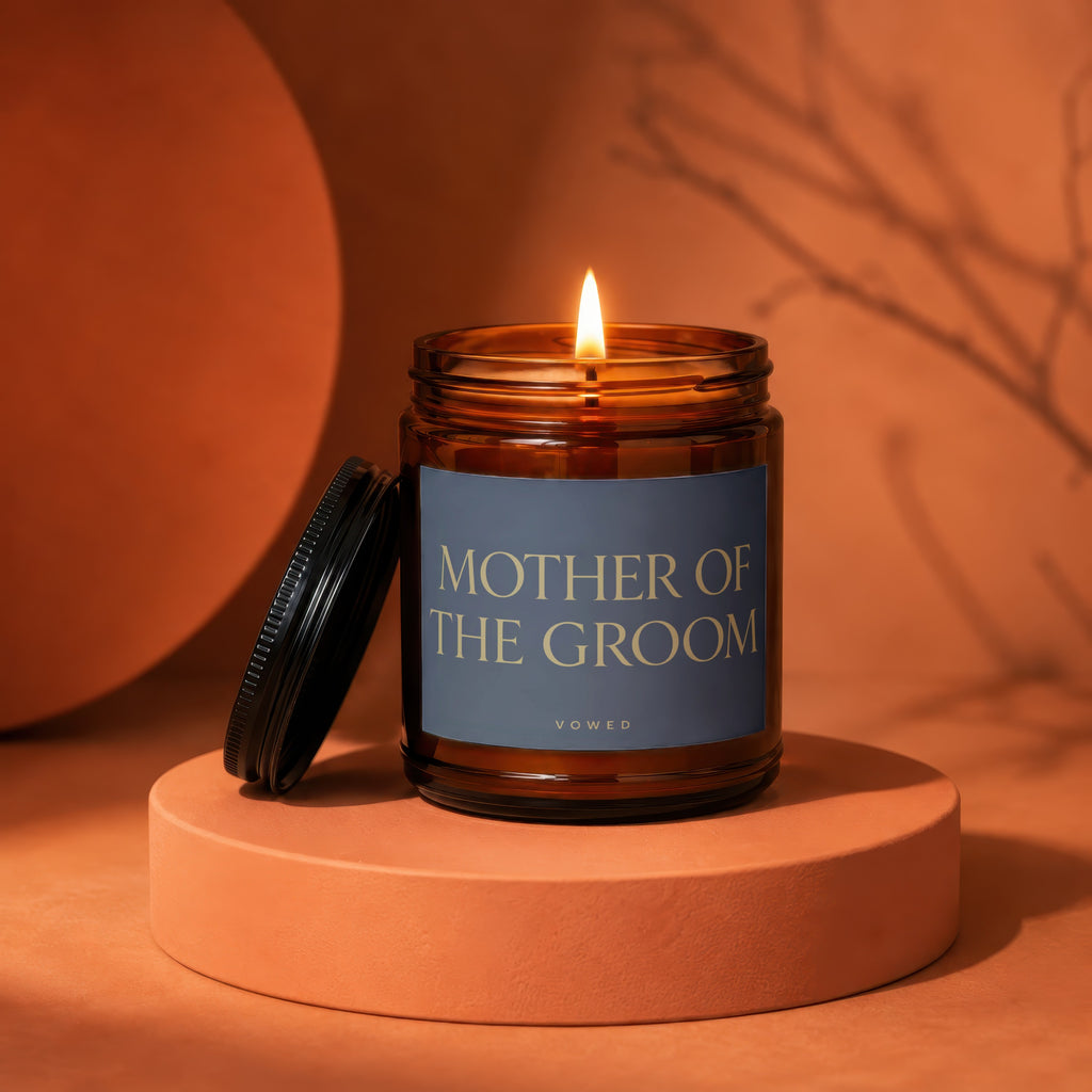 Amber jar candle with lit flame, "MOTHER OF THE GROOM" text, on display stand.