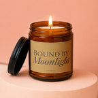 Amber jar candle with lit wick and black lid, reads "Bound by Moonlight Vowed".