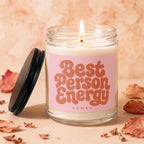 Glass candle with pink label reading "Best Person Energy" and a lit wick.