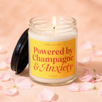Lit candle in glass jar with yellow label that reads "Smells Like Powered by Champagne & Anxiety Vowed".