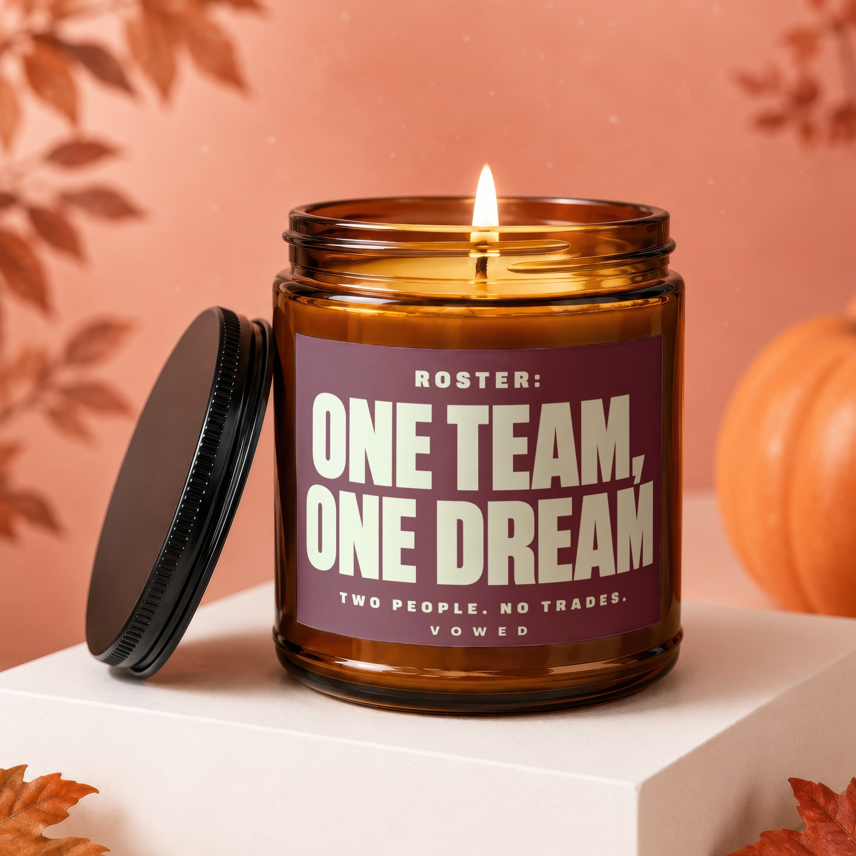 Amber jar candle with lit flame, "ONE TEAM, ONE DREAM" text.