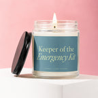 Glass jar candle with "Keeper of the Emergency Kit" text and lit wick.