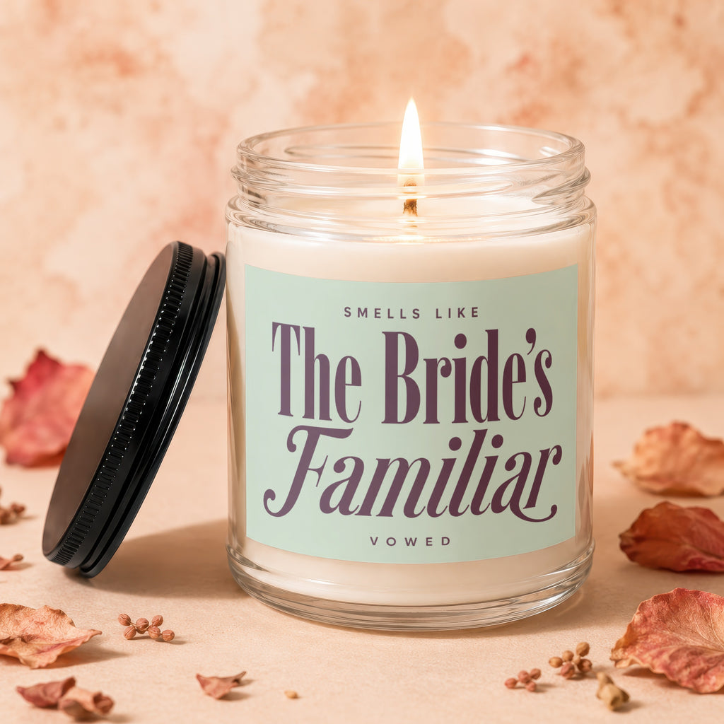 Glass candle with lit flame, labeled "Smells like The Bride's Familiar VOWED".