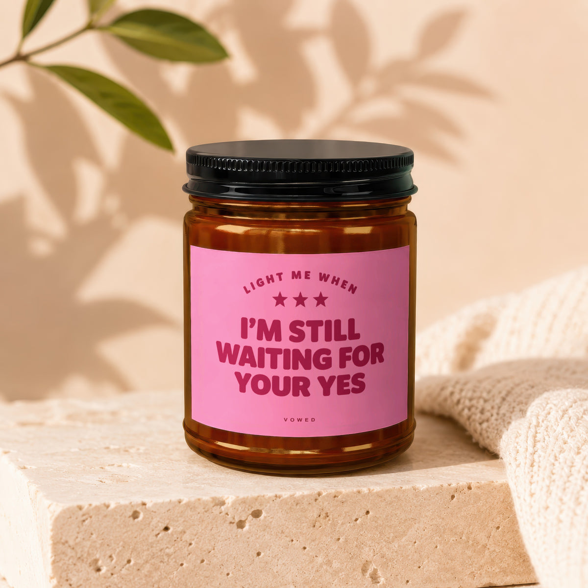 Amber candle with pink label reading "Light me when I'm still waiting for your yes".