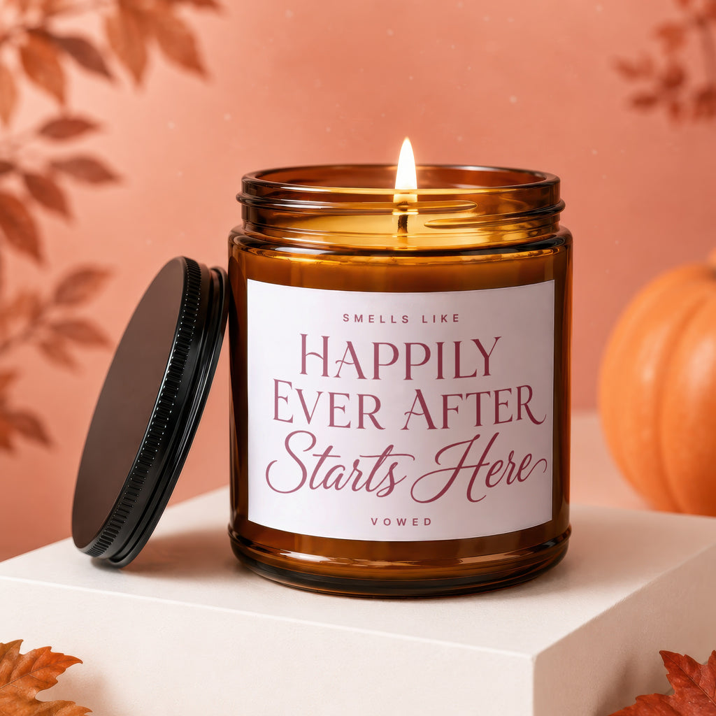 Amber jar candle with lit wick; label reads "Smells Like Happily Ever After Starts Here".