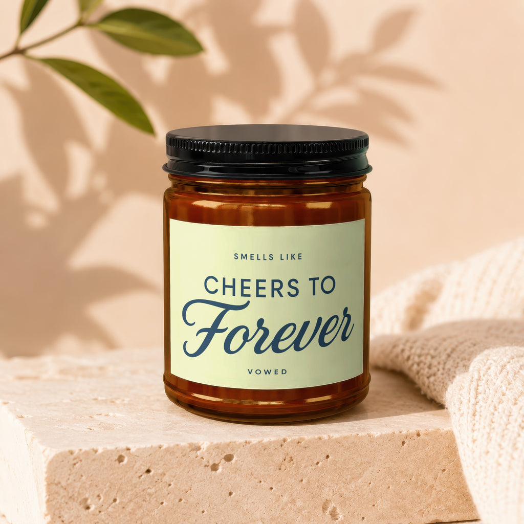 Candle labeled "Cheers to Forever" in amber glass jar with black lid.