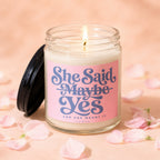 Lit candle with pink label reading "She Said Maybe Yes And She Meant It VOWED".
