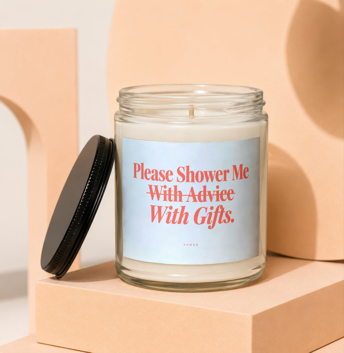 Glass candle with lid off, reading "Please Shower Me With Gifts."