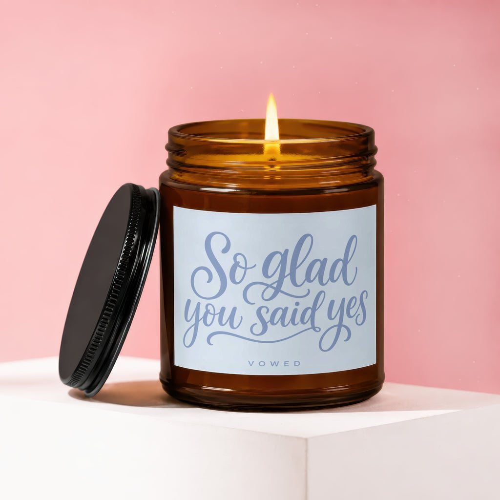 Lit amber glass candle with "So glad you said yes" text and VOWED logo.