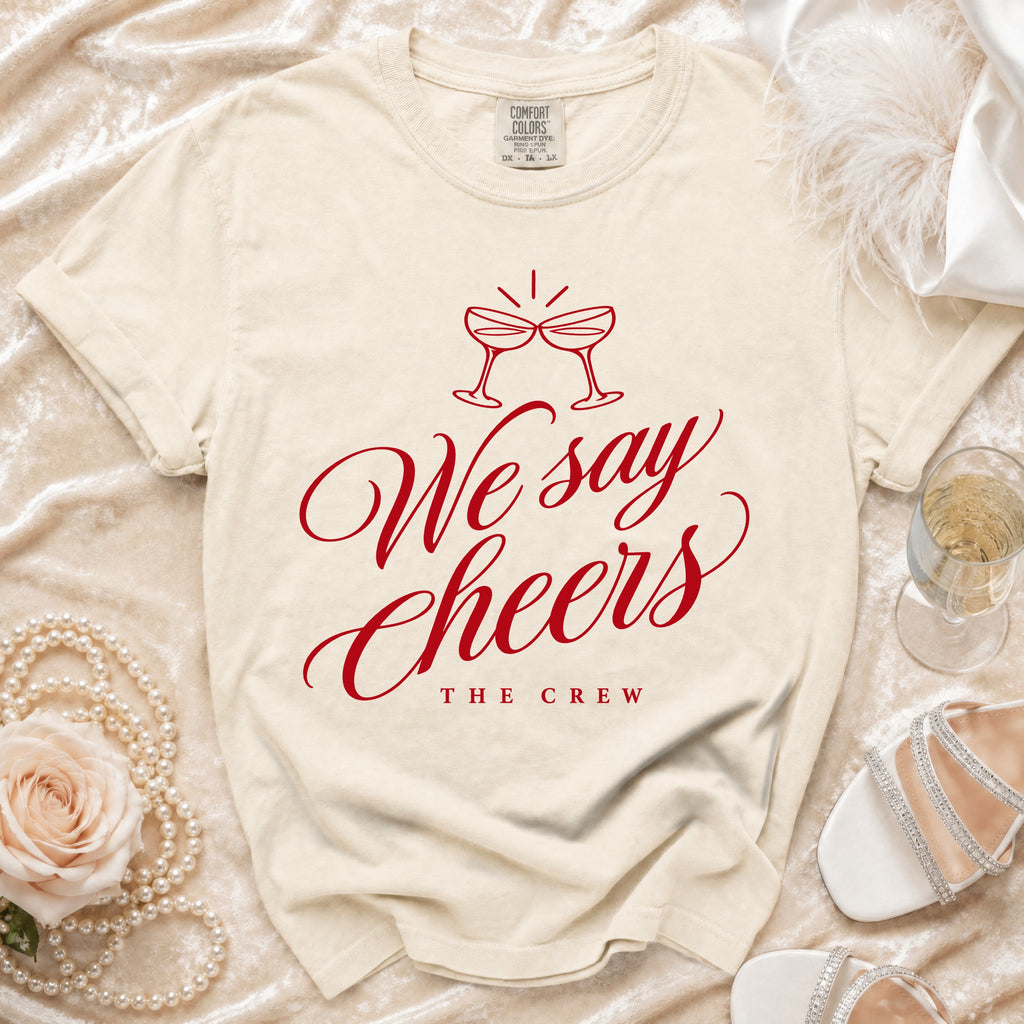 Cream t-shirt with red text "We say Cheers THE CREW" and champagne glasses.