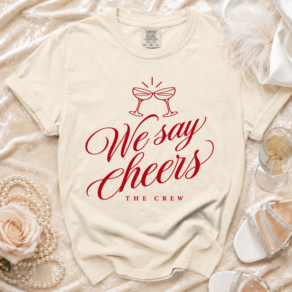 Cream t-shirt with red text "We say Cheers THE CREW" and champagne glasses.