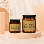 Two amber glass candles with black lids labeled "Bound by Moonlight".