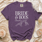 Purple t-shirt with "BRIDE & BOOS Social" text and skeleton hands toasting champagne.