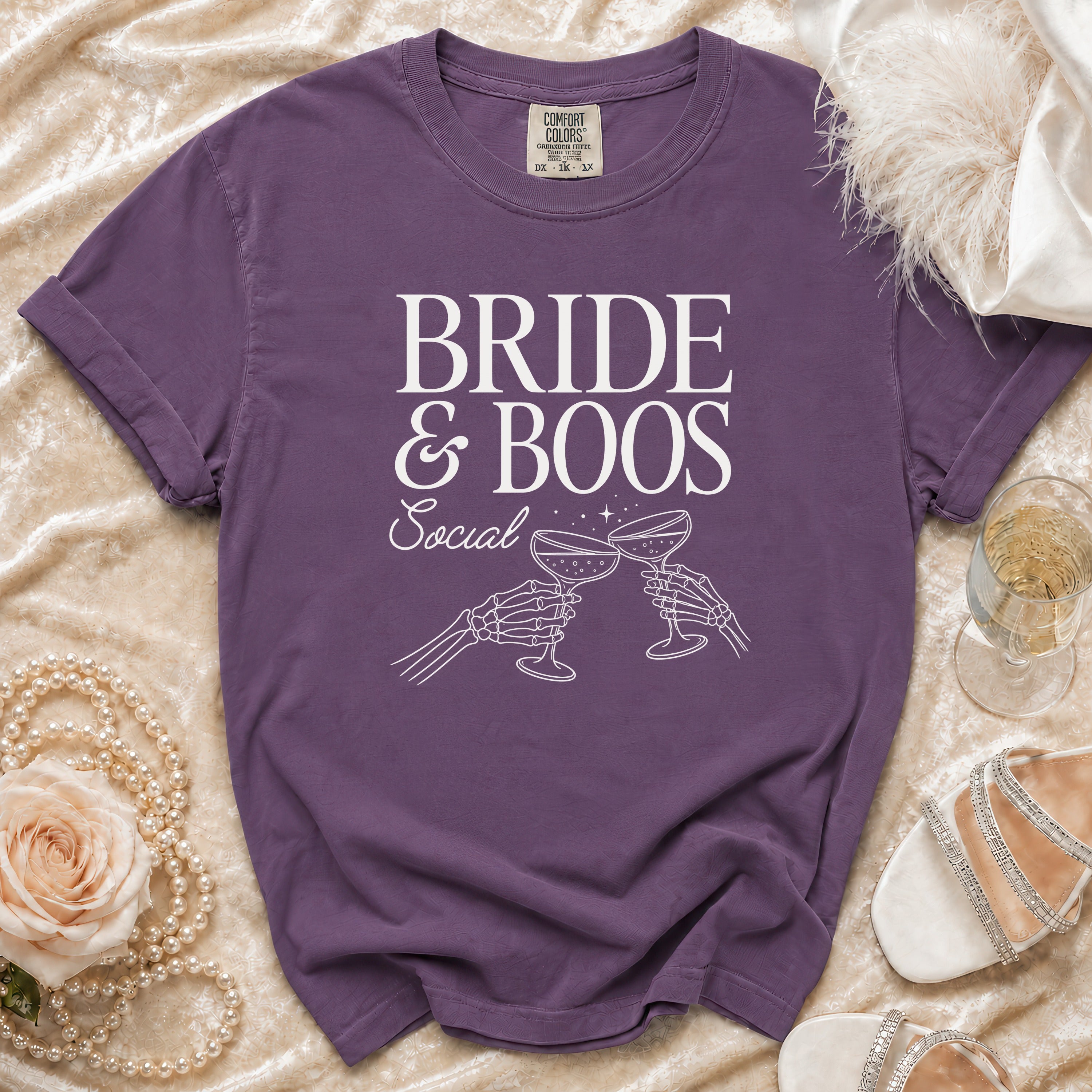 Purple t-shirt with "BRIDE & BOOS Social" text and skeleton hands toasting champagne.