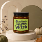 Candle with "Skeptical Honorary Witch" text on a light green label.