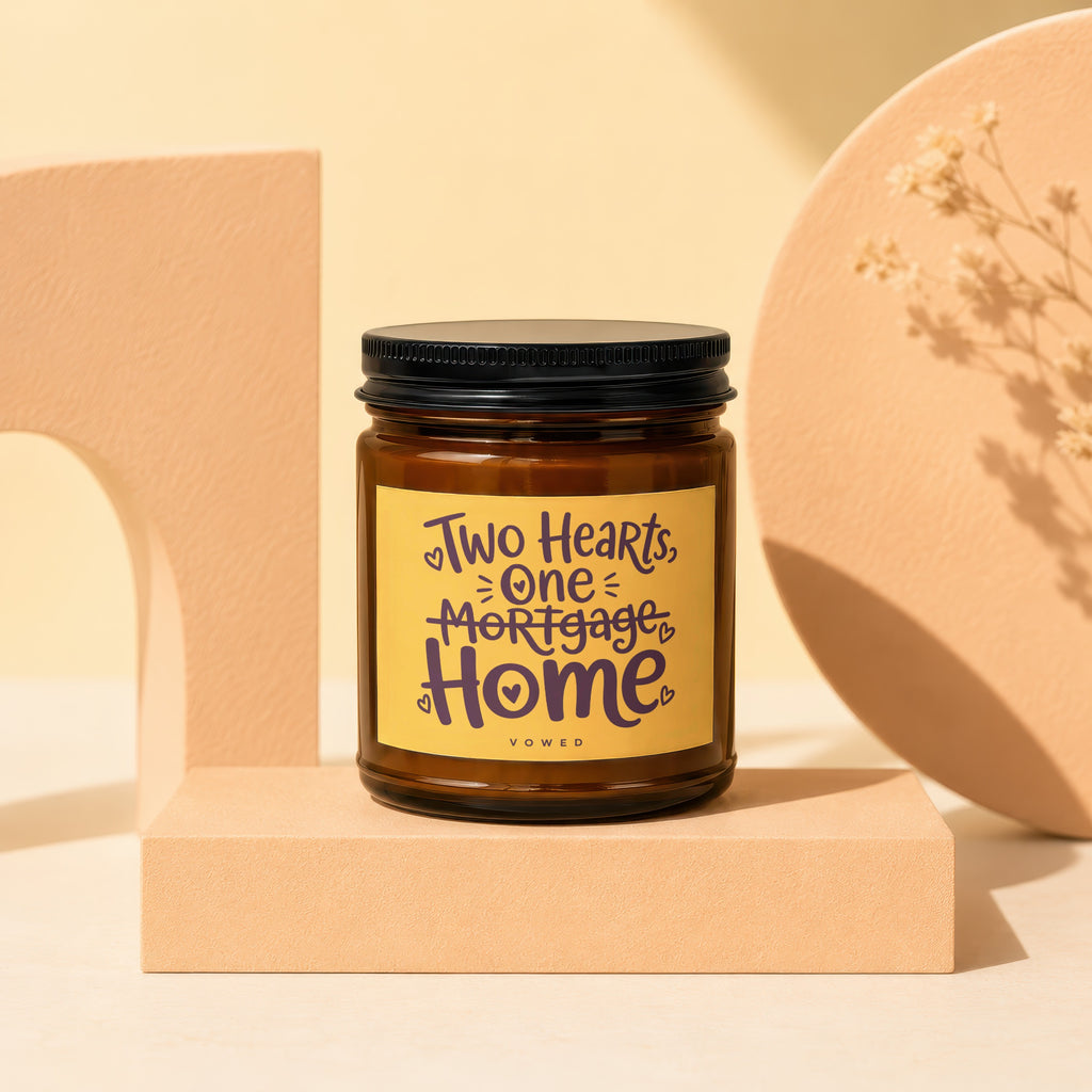 Brown glass candle with yellow label reading "Two Hearts, One Mortgage Home".