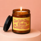 Amber candle with lit wick and text "Our Love Story Ends Continues".
