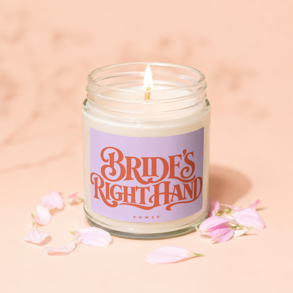 Lit candle in a glass jar with text "BRIDE'S RIGHT HAND VOWED" and pink petals.