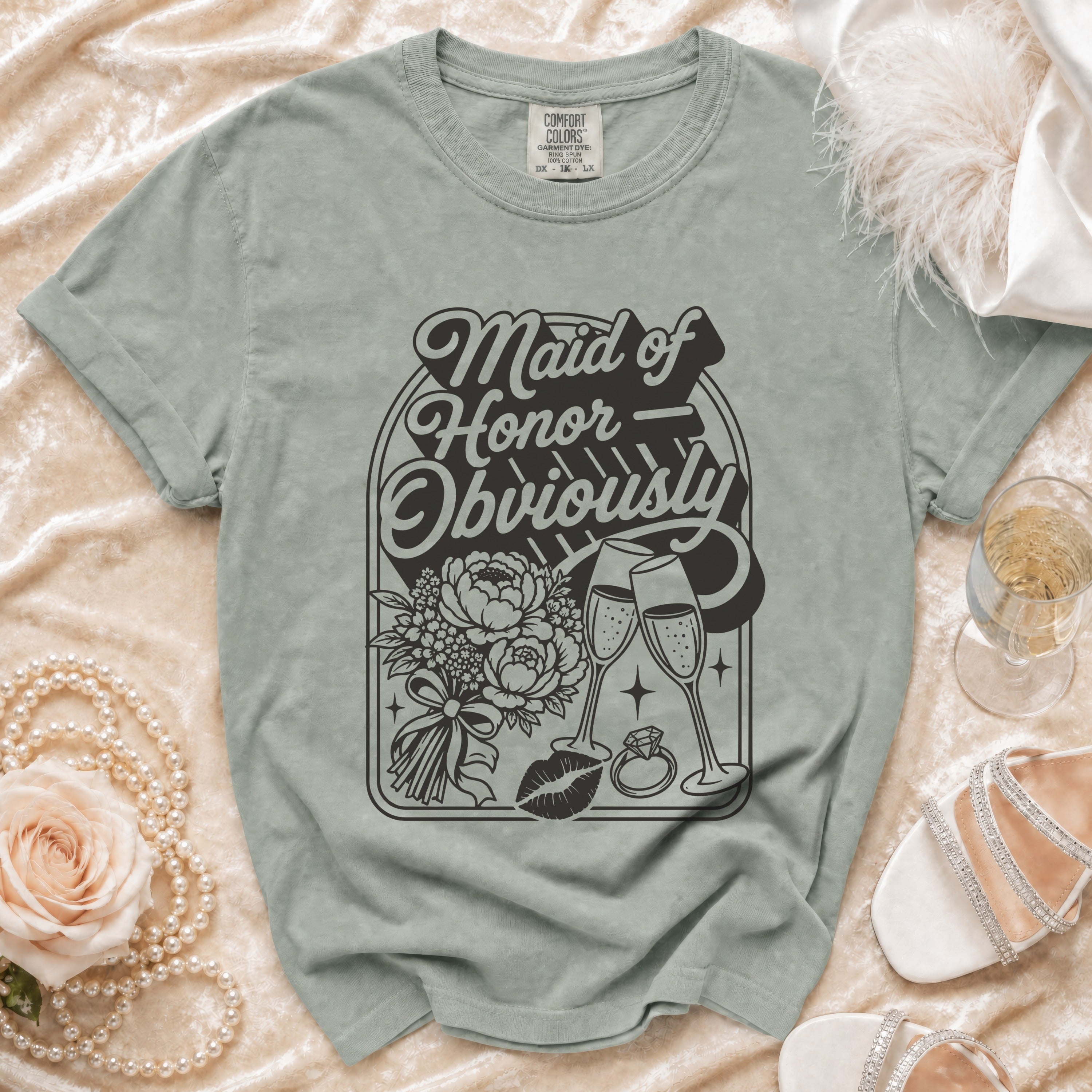 Maid of Honor Obviously t-shirt with floral bouquet, champagne glasses, lipstick, and ring graphic.