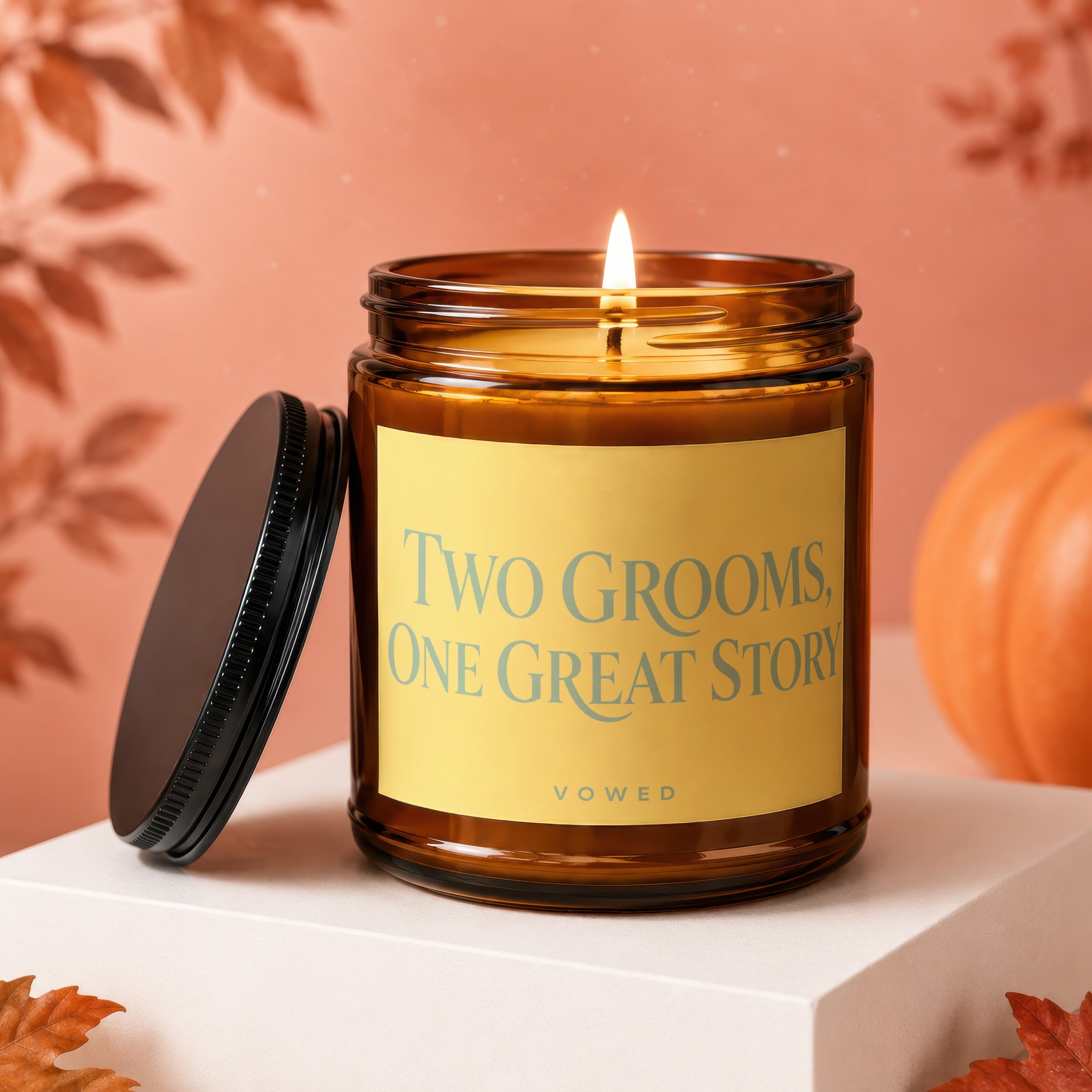 Lit amber glass candle with lid off, reads "Two Grooms, One Great Story".