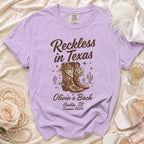 Purple t-shirt with "Reckless in Texas" and cowboy boots graphic.
