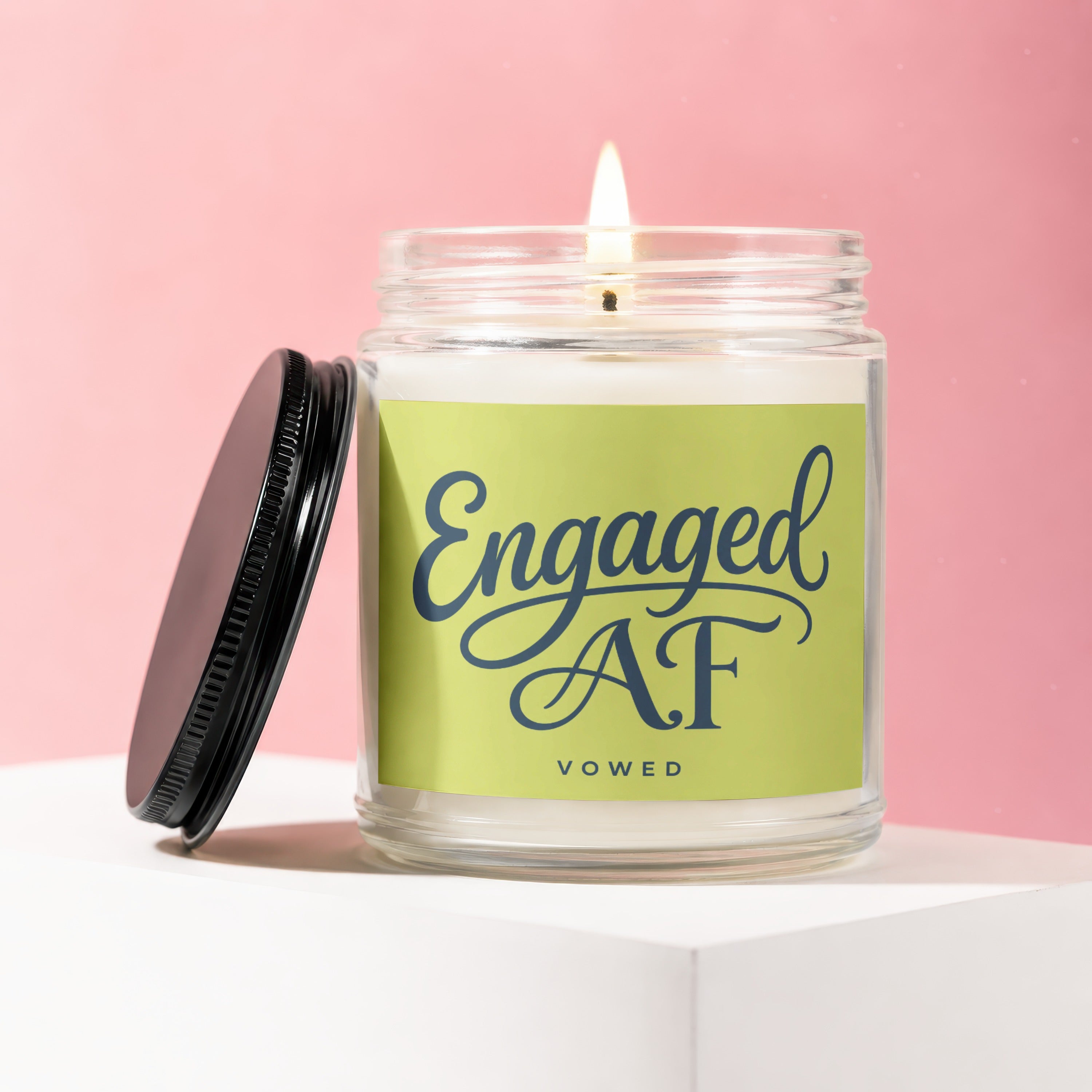 Glass candle with lit wick, green label reading "Engaged AF VOWED".