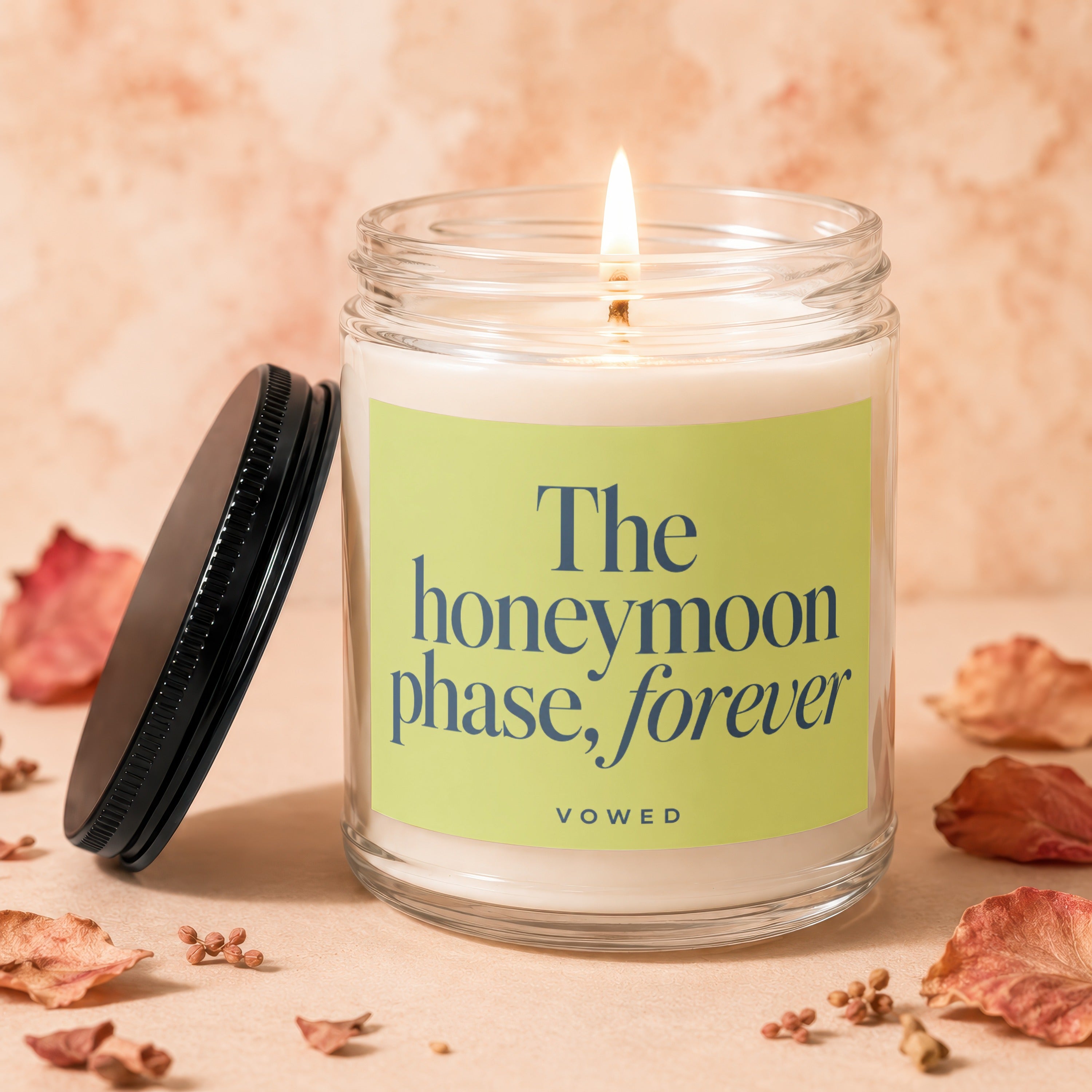 Glass candle with lid off, burning flame, and "The honeymoon phase, forever" text.