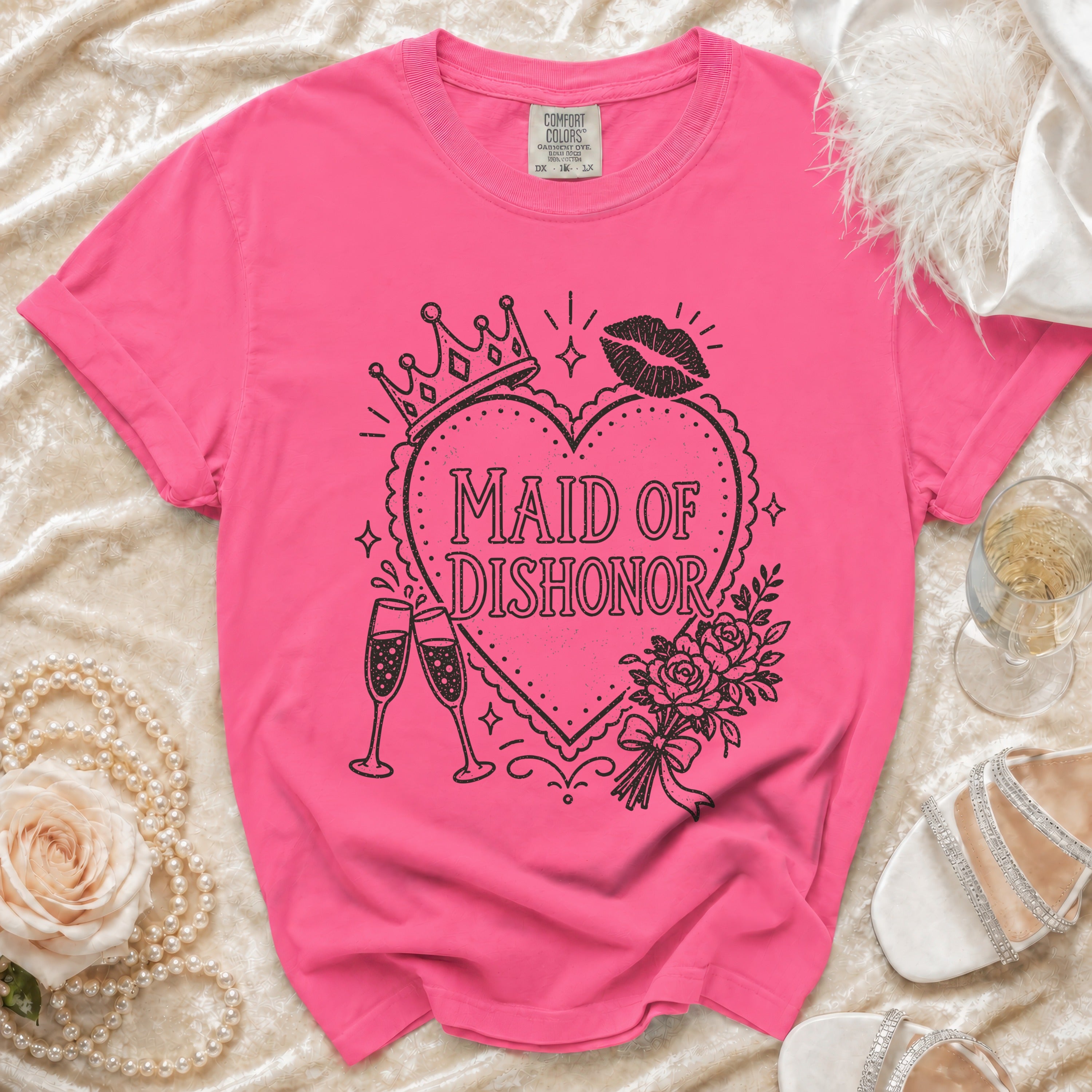 Pink t-shirt with "Maid of Dishonor" text, crown, lipstick, and champagne glasses graphic.