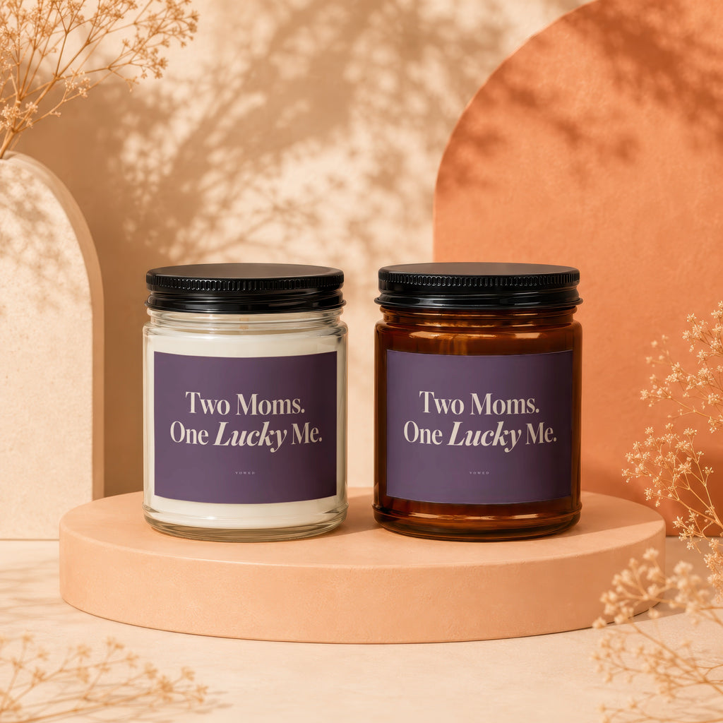 Two candles with "Two Moms. One Lucky Me." text on purple labels.
