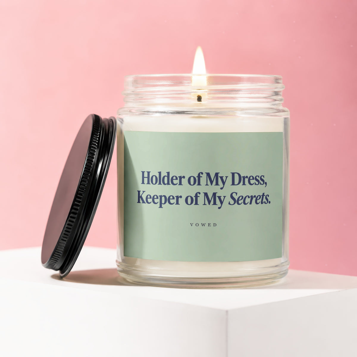 Candle with lit wick and black lid, labeled "Holder of My Dress, Keeper of My Secrets. VOWED."