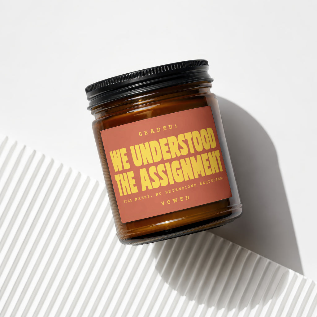 Amber jar candle with a burnt orange label that reads "WE UNDERSTOOD THE ASSIGNMENT".