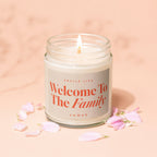 Glass jar candle with lit wick. Label reads 'Smells Like Welcome To The Family'.