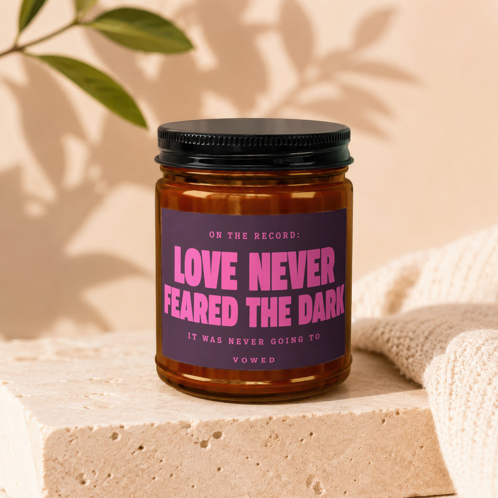 Amber jar candle with black lid, purple label reading "Love Never Feared The Dark" and "Vowed".