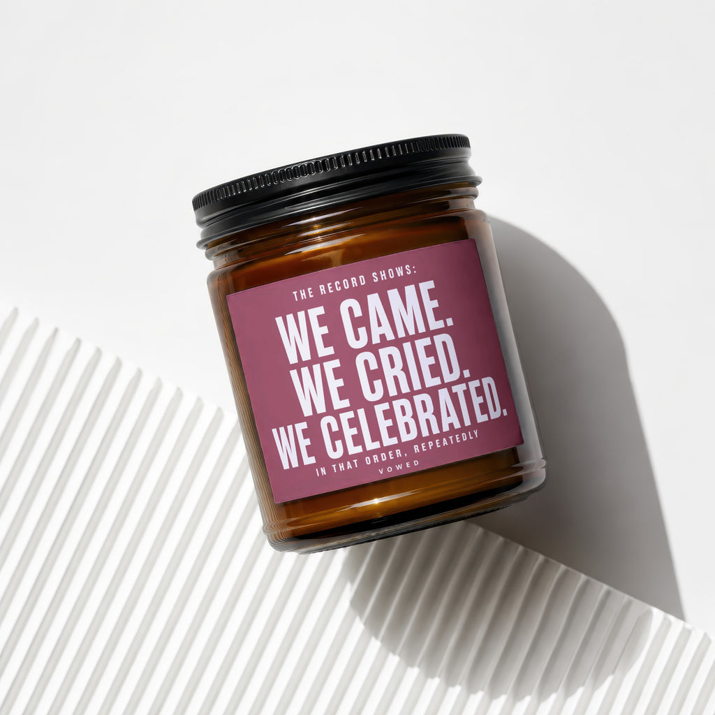 Amber jar candle with black lid and a maroon label reading "WE CAME. WE CRIED. WE CELEBRATED."