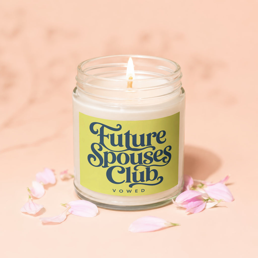 Lit candle in glass jar with "Future Spouses Club" label surrounded by pink flower petals.