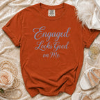Orange t-shirt with blue rhinestone text "Engaged Looks Good on Me".