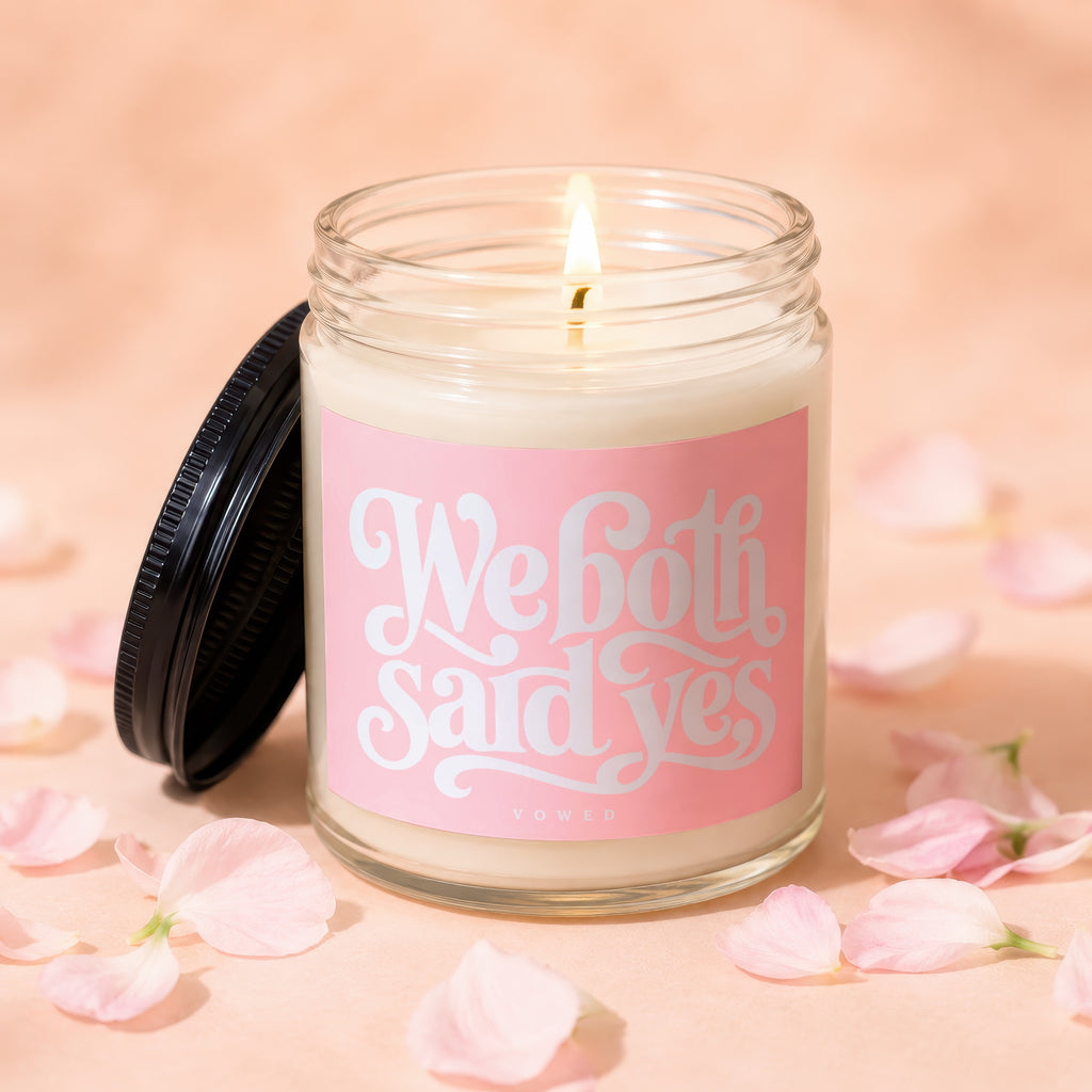 Lit candle in glass jar with pink label saying "We both said yes VOWED".