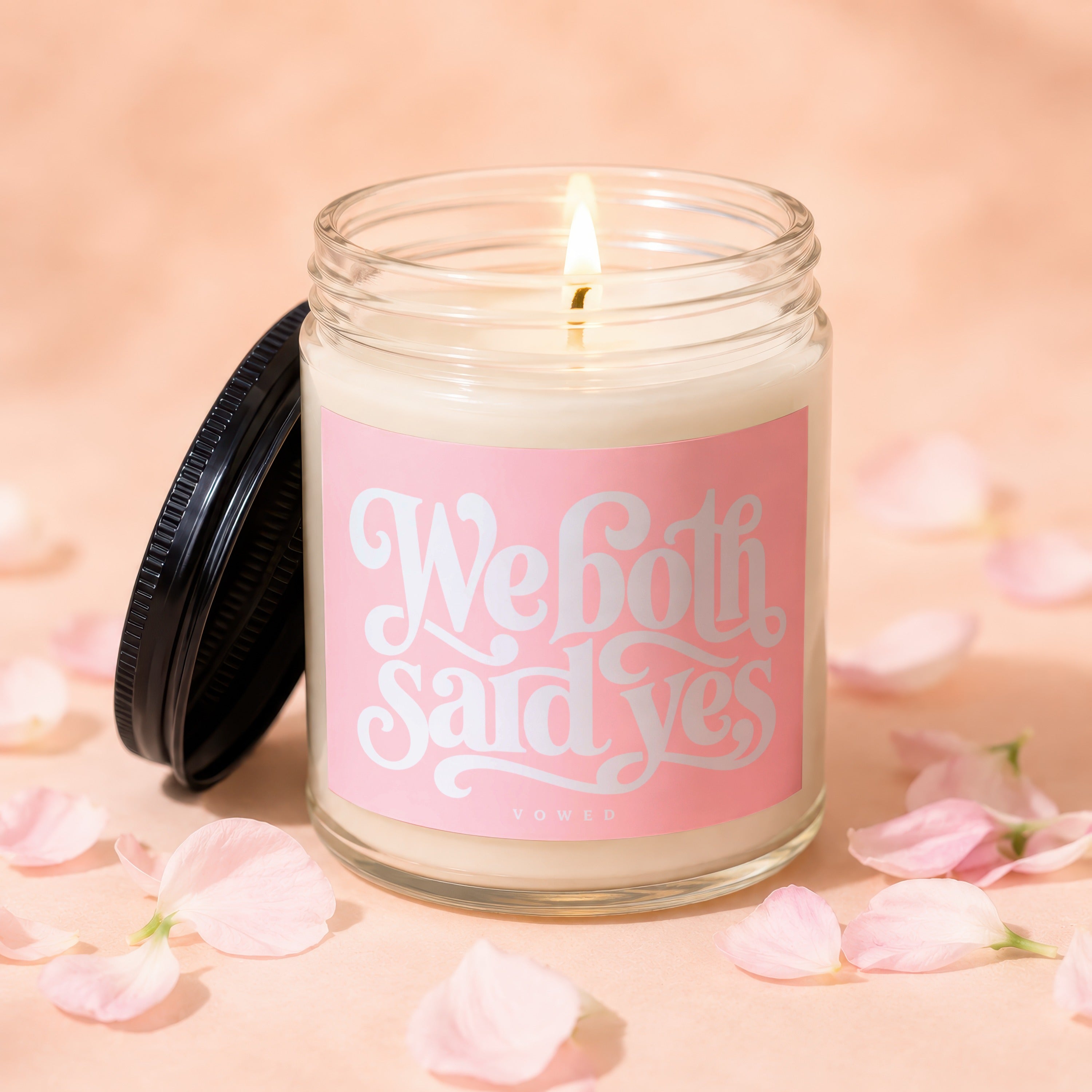 Lit candle in glass jar with pink label saying "We both said yes VOWED".
