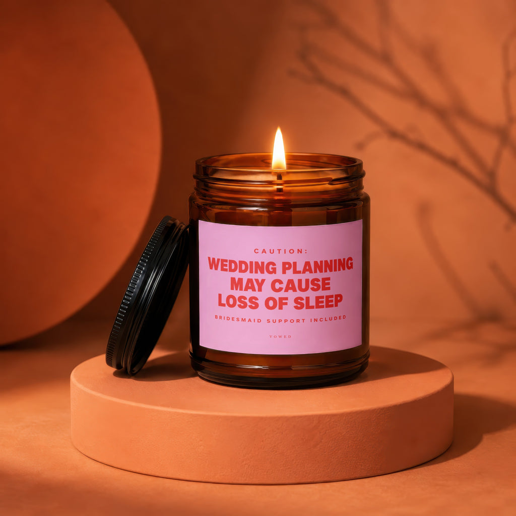 Amber candle with lit wick and pink label reading "Wedding planning may cause loss of sleep."
