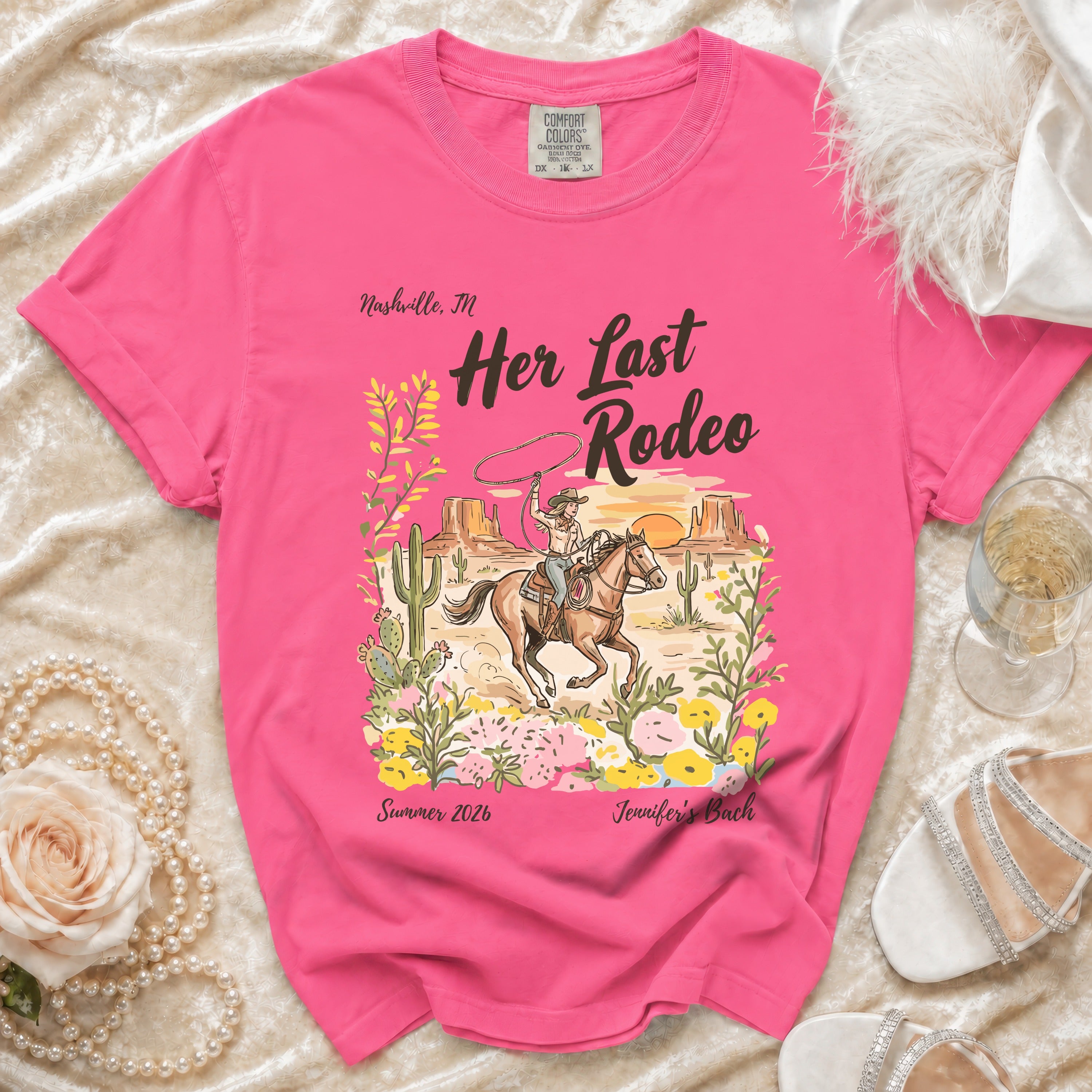 Pink t-shirt with "Her Last Rodeo" graphic, cowboy on horse, cactus, flowers, and text.